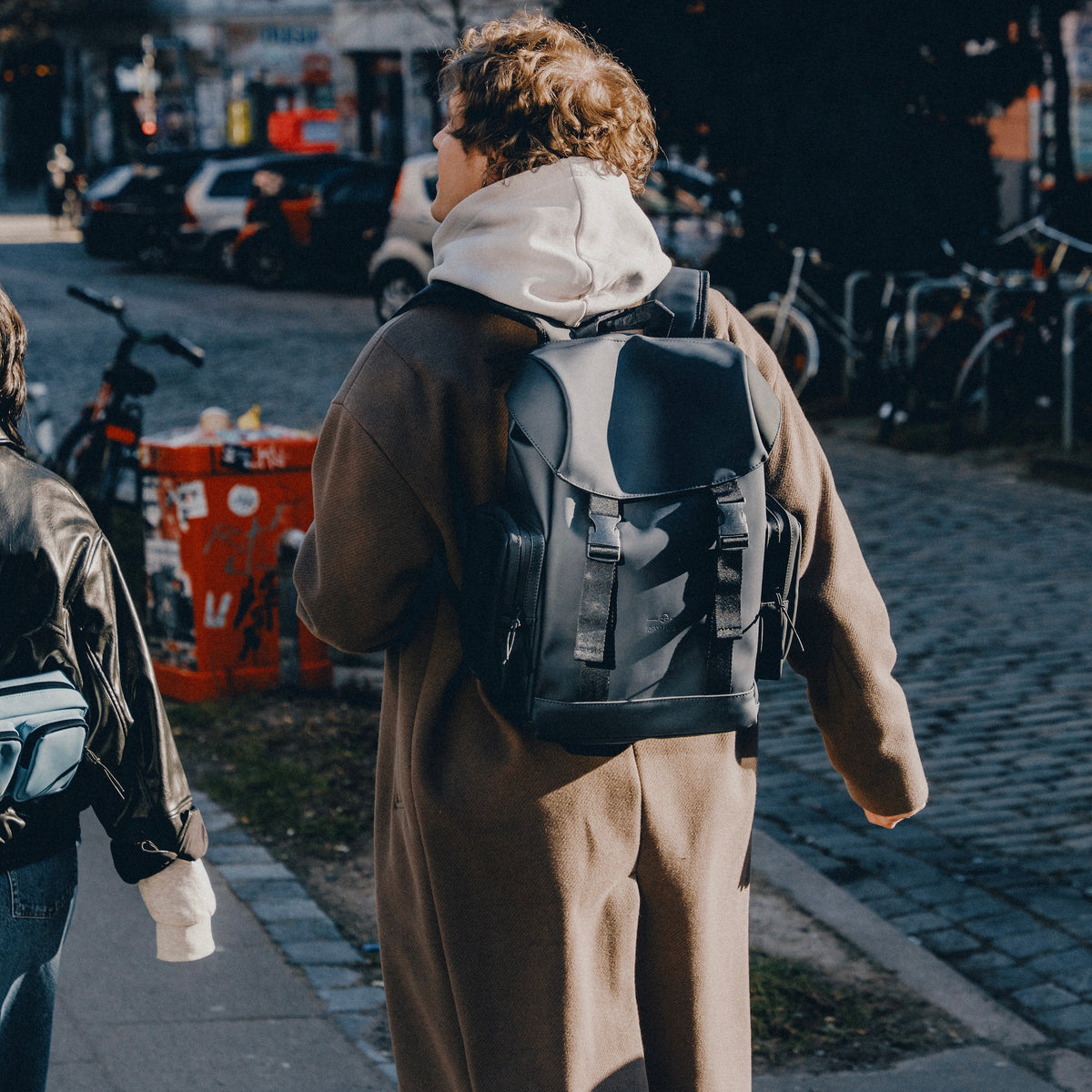 Person trägt braunen Mantel und schwarzen Rucksack 'Finley' beim Gehen in der Stadt