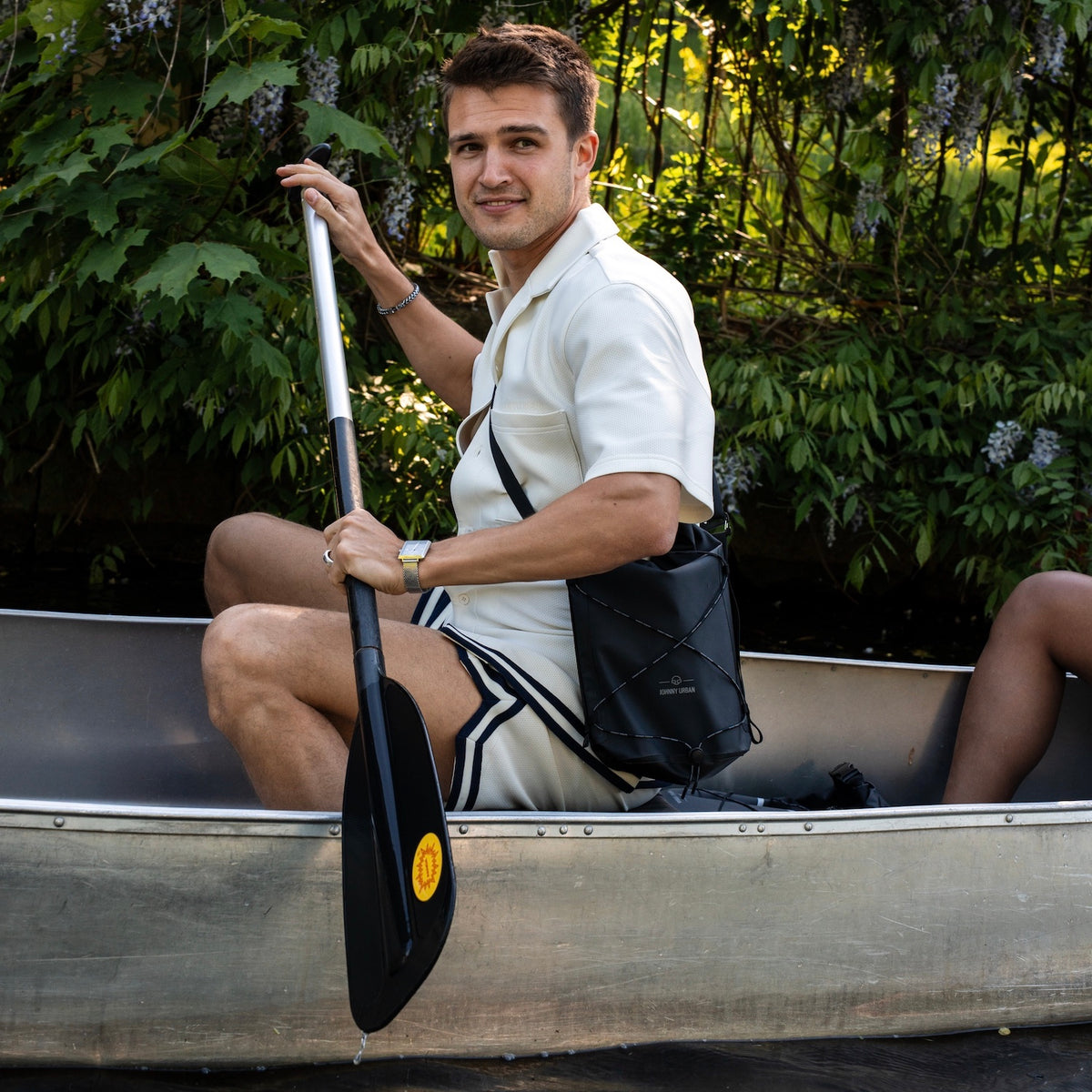 Mann sitzt in einem Kanu, hält ein Paddel und trägt die wasserdichte Dry Bag 'Theo' von Johnny Urban in Schwarz