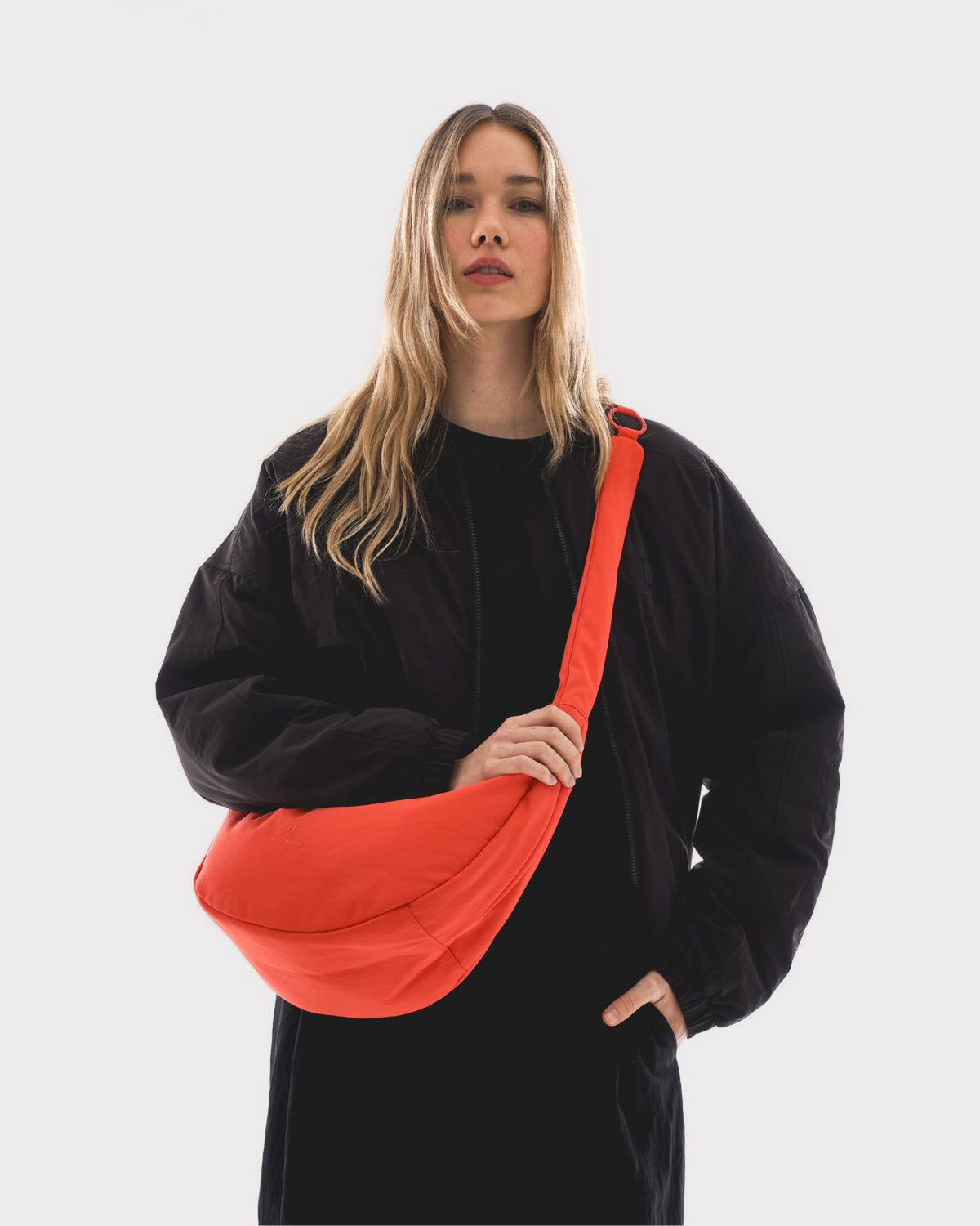 Unser weibliches Model präsentiert sich hier mit der Half-Moon-Bag "Lou Large" in coral-rot.