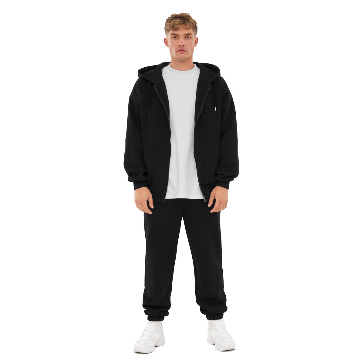 Mann trägt schwarze Jogginghose 'Owen' von Johnny Urban mit weißem T-Shirt, schwarzer Zip-Hoodie und weißen Sneakern