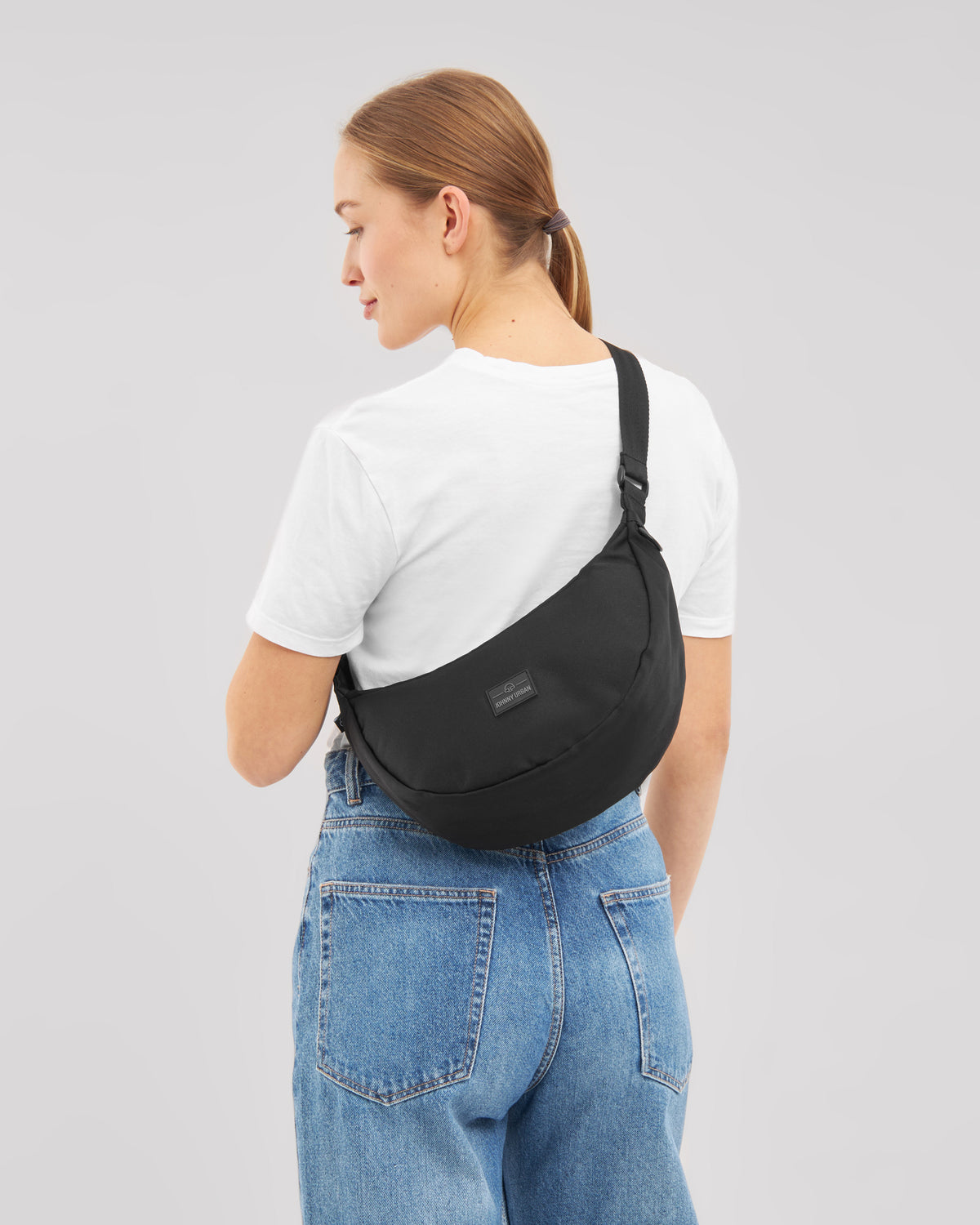 Frau von hinten mit schwarzer Half Moon Umhängetasche 'Ally Medium', weißem T-Shirt und blauen Jeans