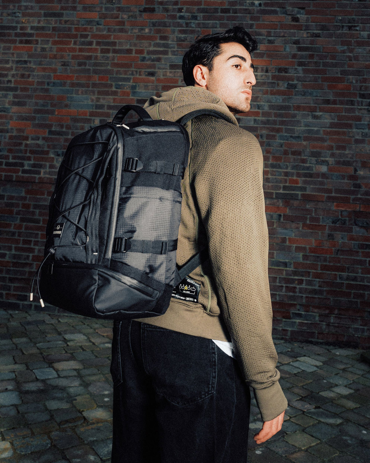 Mann trägt schwarzen Rucksack 'Jack' von Johnny Urban vor Ziegelsteinmauer
