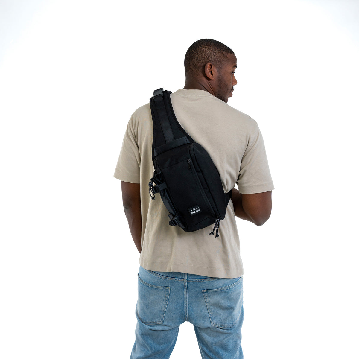 Mann mit beigem T-Shirt und blauer Jeans trägt schwarze Johnny Urban Sling Bag 'Charlie' über den Rücken