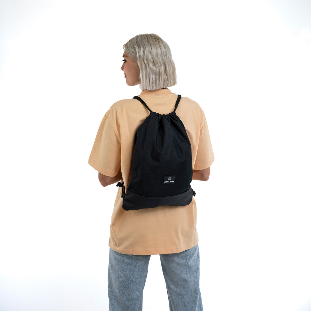Frau mit kurzem blonden Haar trägt den schwarzen Turnbeutel 'Blake' von Johnny Urban auf dem Rücken
