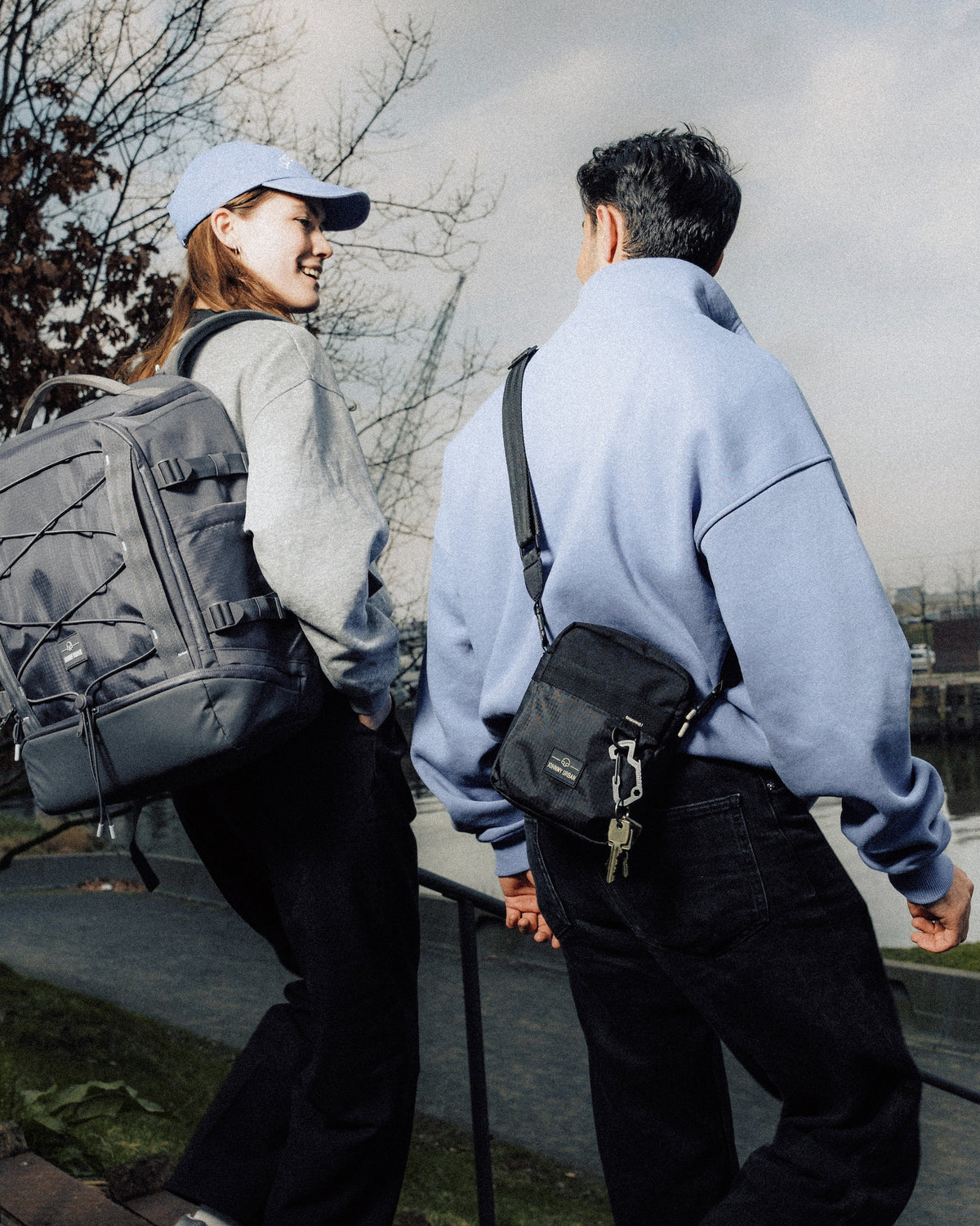 Zwei Personen gehen außen, eine trägt grauen Rucksack, andere schwarze Umhängetasche 'Jayden'