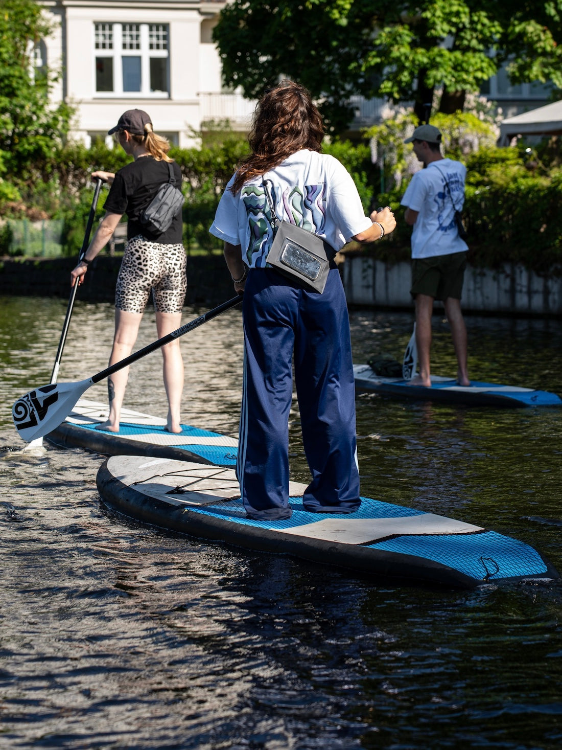 Frau steht auf einen Sup mit einem Paddel in der Hand und trägt eine wasserfeste Tasche.