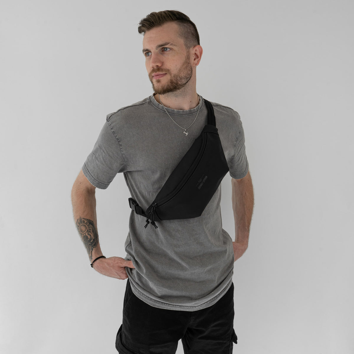 Mann mit grauem T-Shirt trägt die schwarze Bauchtasche 'Riley' von Johnny Urban diagonal über der Brust