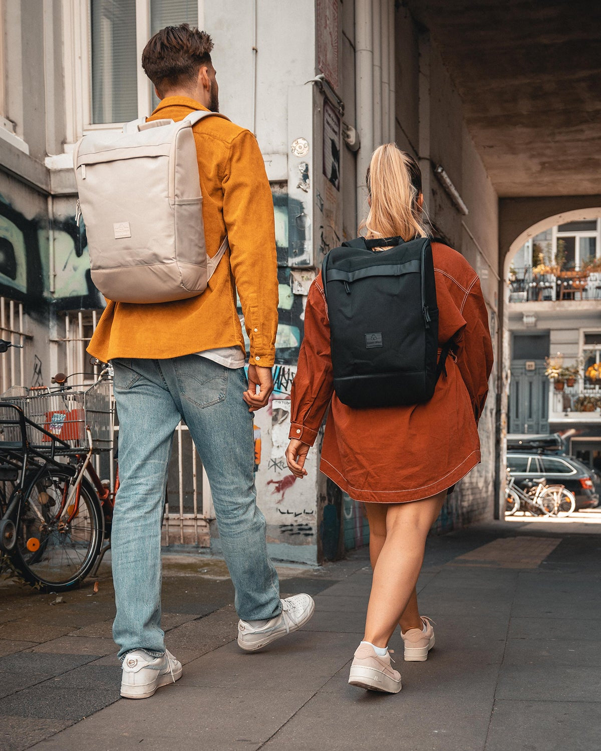 Zwei Personen gehen durch einen Stadtdurchgang, tragen Business Rucksäcke 'Jasper' in Beige und Schwarz