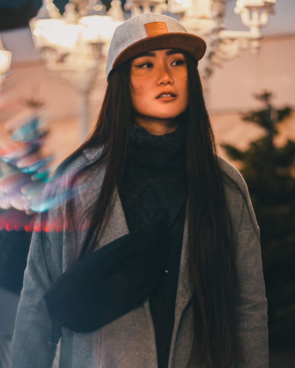 Frau mit langer Haaren, grauem Mantel, grauer Kappe und schwarzer Bauchtasche 'Tom' von Johnny Urban