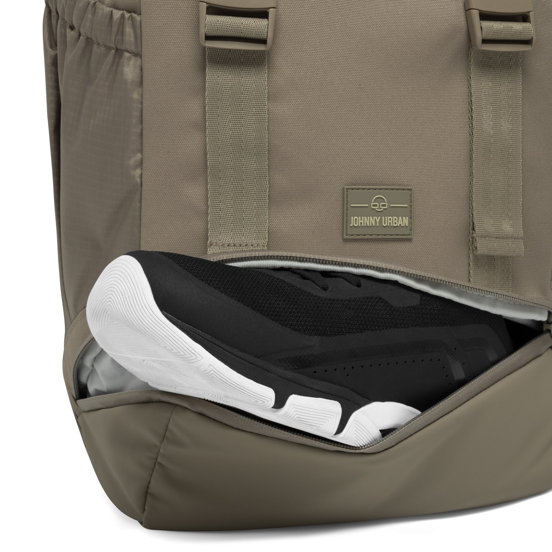 Johnny Urban Rucksack 'Nico' in desertgrau mit seitlichem Fach, das schwarze Sneaker mit weißer Sohle hält