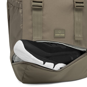 Johnny Urban Rucksack 'Nico' in desertgrau mit seitlichem Fach, das schwarze Sneaker mit weißer Sohle hält
