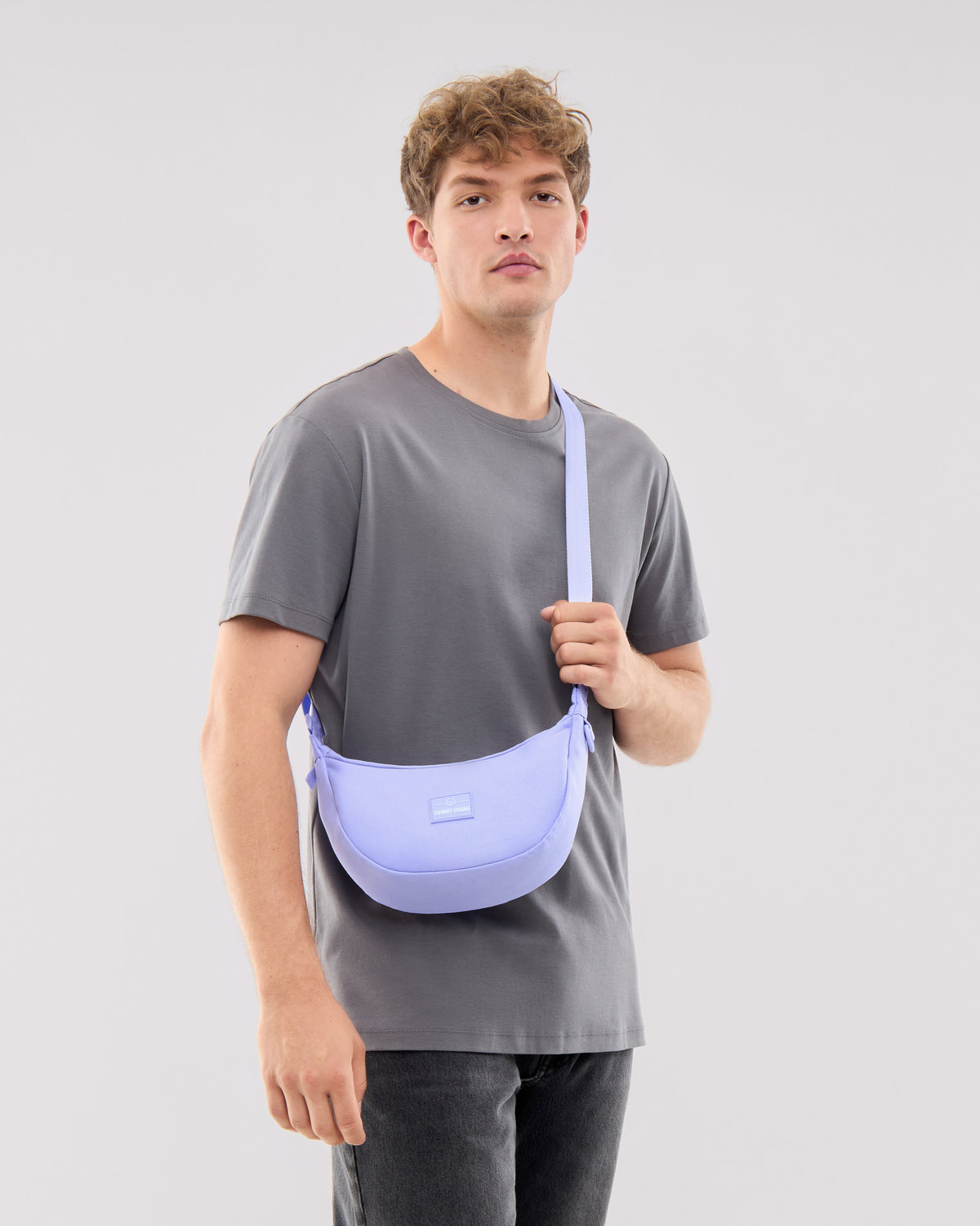 Mann trägt Half Moon Bag ‚Ally Small‘ in fliederfarbenem Nylon als Umhängetasche