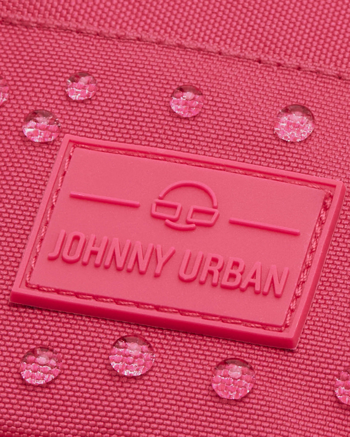 Nahaufnahme der wasserabweisenden pinkfarbenen Umhängetasche 'Josh' von Johnny Urban mit sichtbaren Wassertropfen und Markenlogo