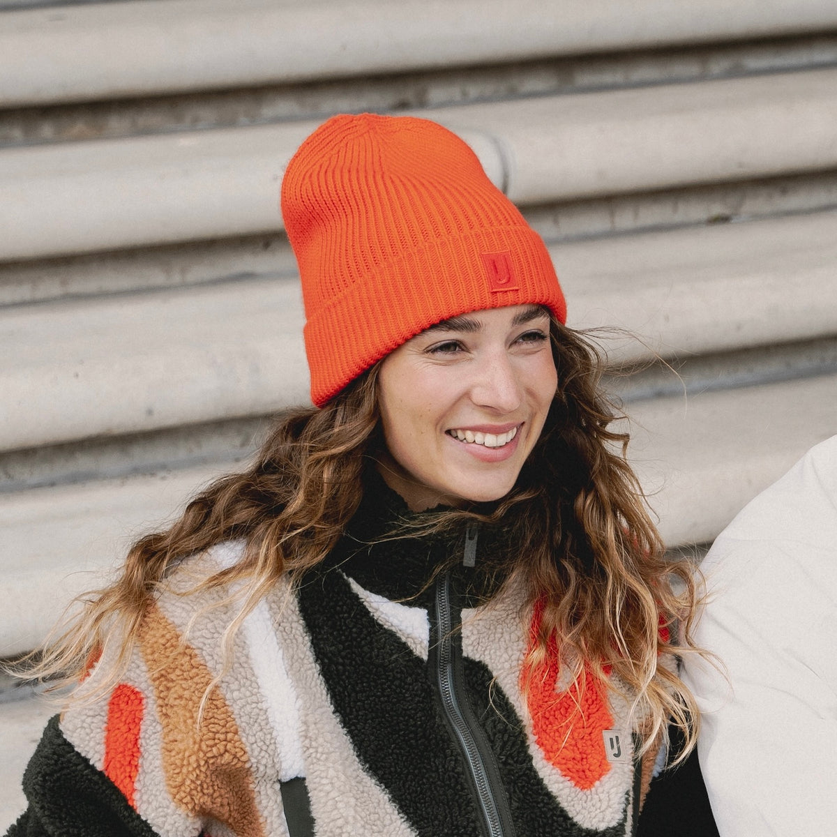 Eine Frau mit der coral farbigen Mützen Billie lächelt in die Kamera