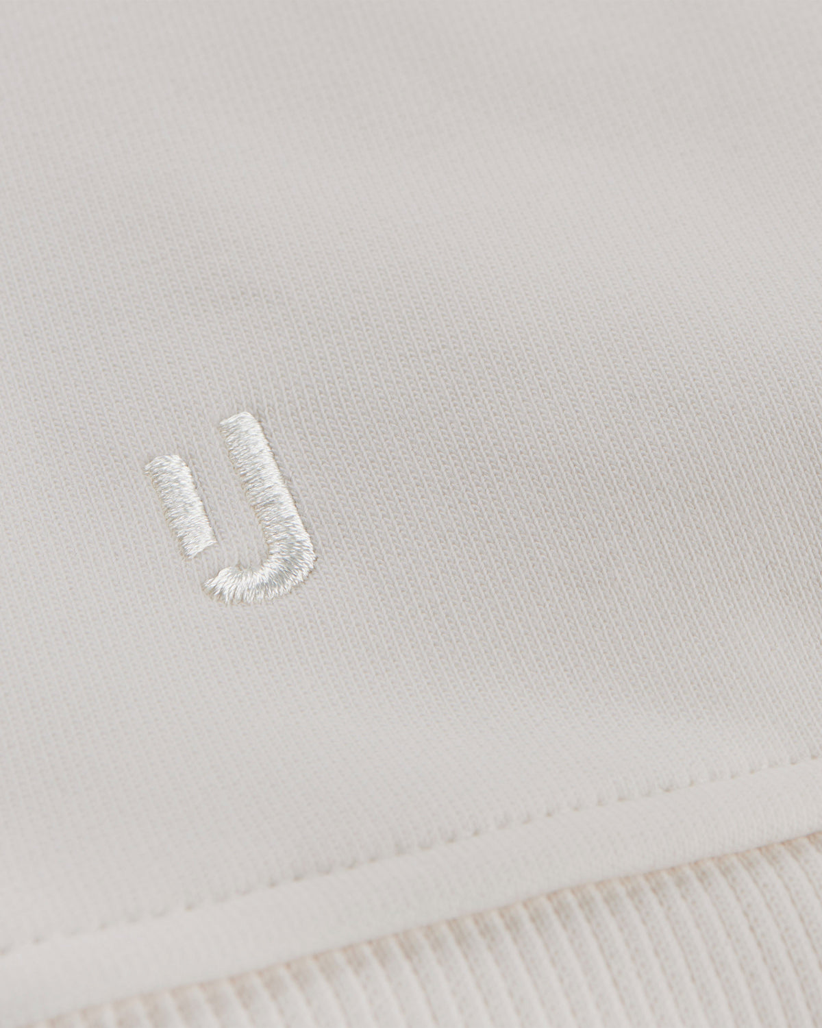 Nahaufnahme des cremefarbenen Oversized Crewnecks 'Carter' von Johnny Urban mit weißem gesticktem Logo