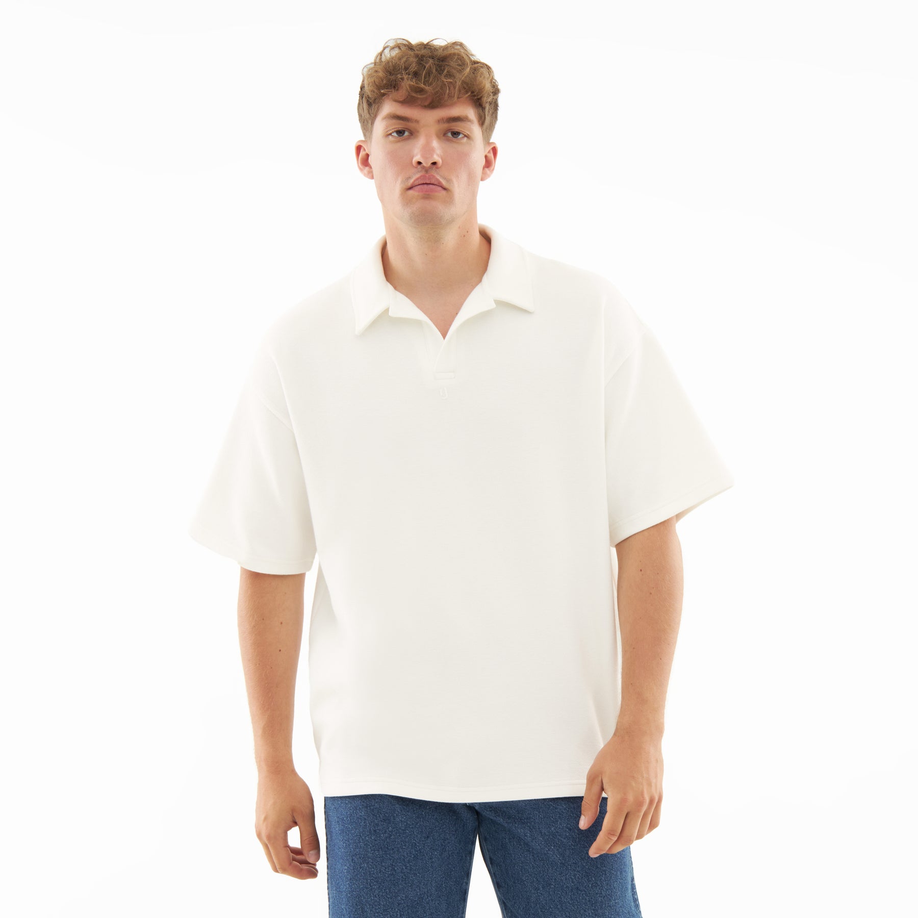 Mann trägt cremefarbenes Herren-Polohemd mit kurzem Arm und offenem Kragen, kombiniert mit blauen Jeans