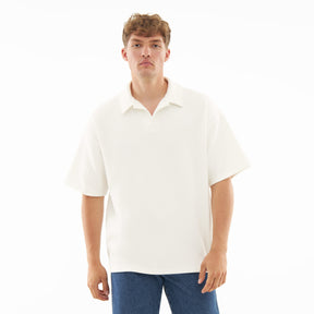 Mann trägt cremefarbenes Herren-Polohemd mit kurzem Arm und offenem Kragen, kombiniert mit blauen Jeans