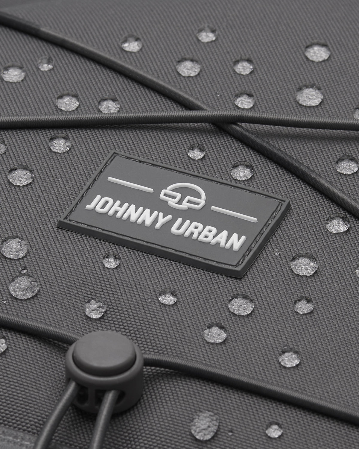 Nahaufnahme des grauen, wasserabweisenden Reiserucksacks 'Allen Large Travel' von Johnny Urban mit Wasserperlen auf der Oberfläche