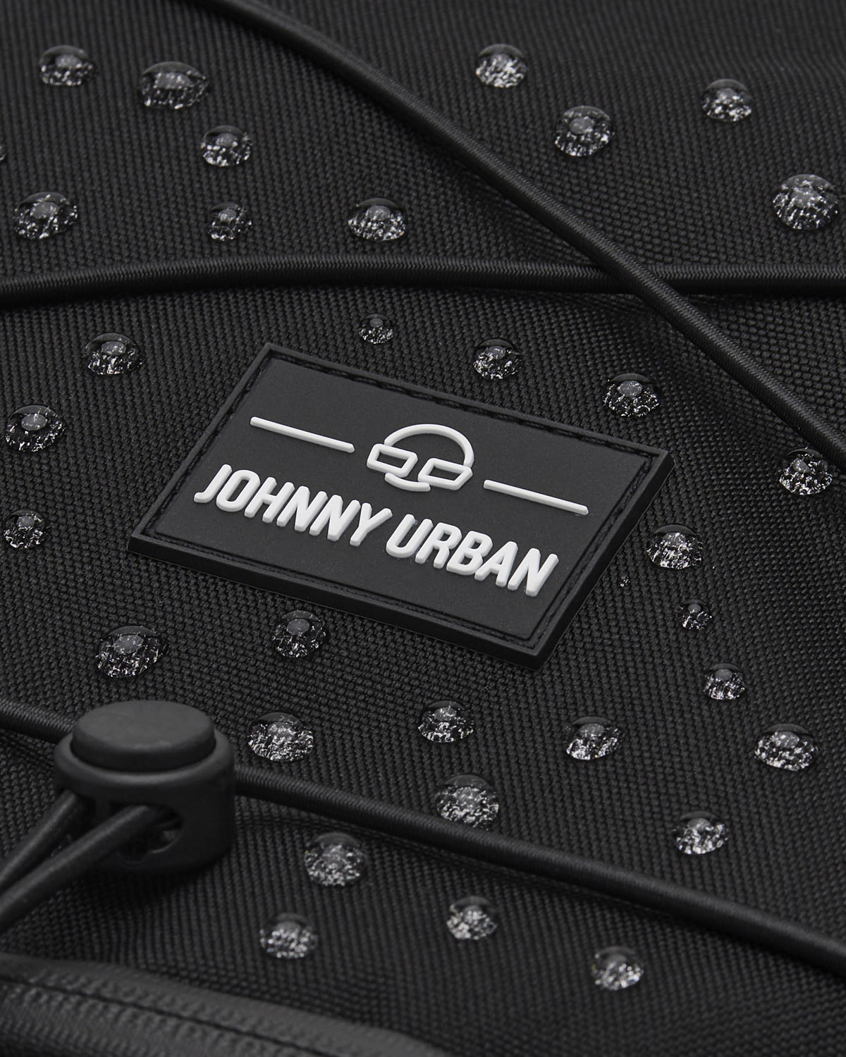 Nahaufnahme des schwarzen wasserabweisenden Reiserucksacks 'Allen XL Travel' mit JOHNNY URBAN Logo und Wassertropfen