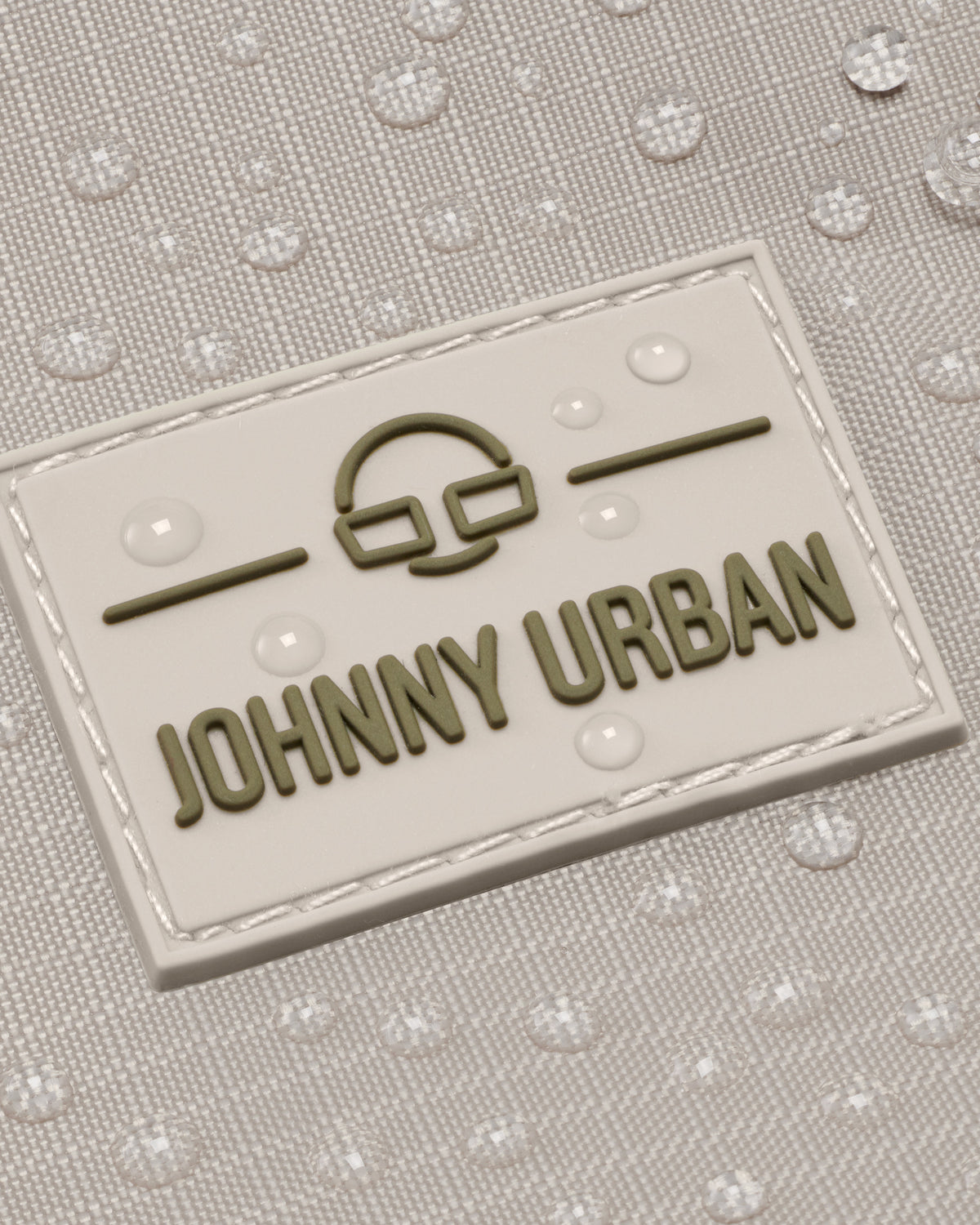 Johnny Urban Markenlogo auf wasserabweisendem beigem Rucksackmaterial mit Wassertropfen