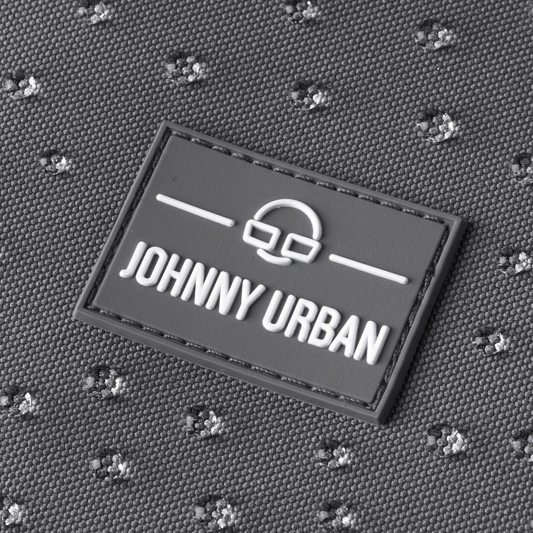 Nahaufnahme des Johnny Urban Logos auf einem dunklgrauen, wasserfesten Rucksack Mo mit strukturiertem Stoff