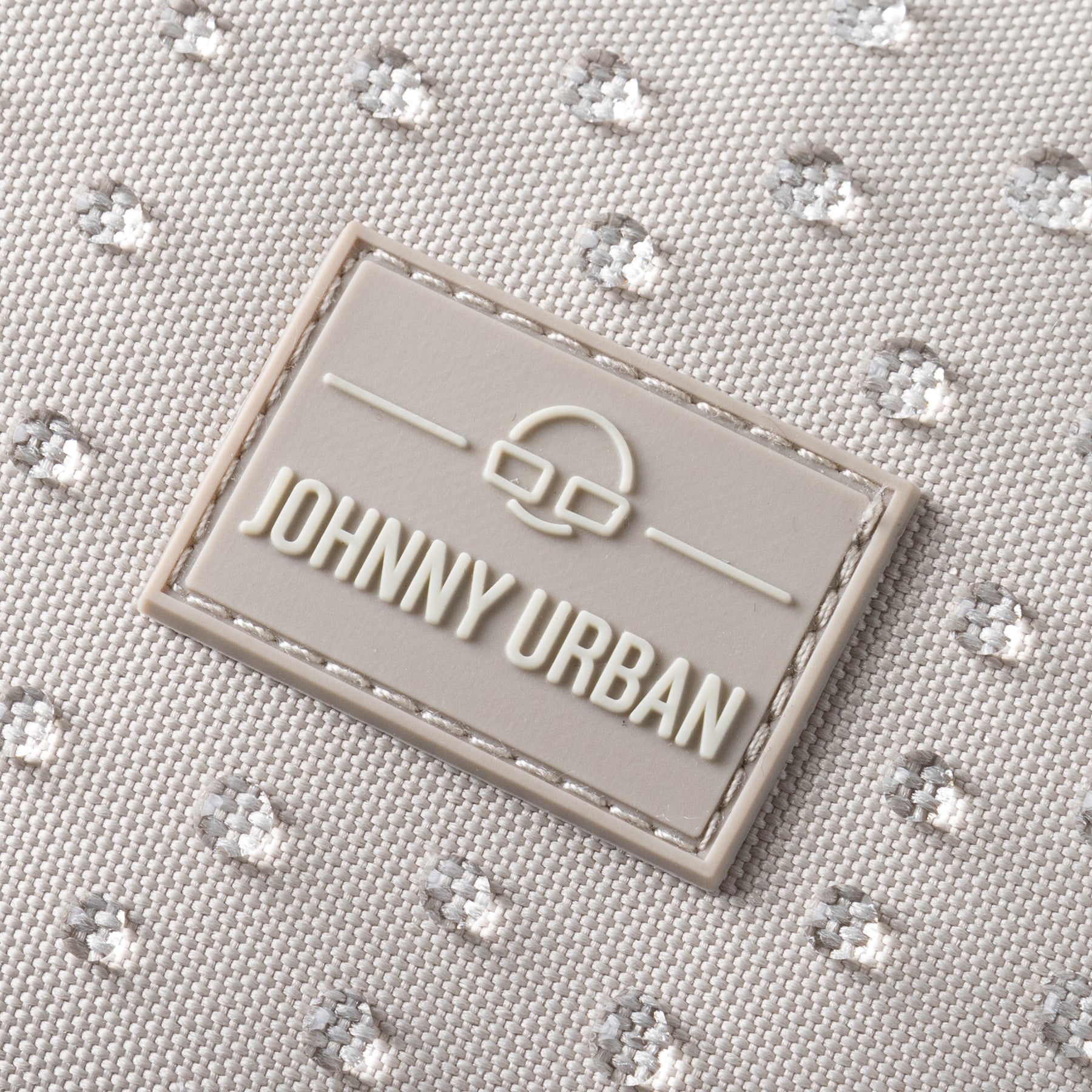 Nahaufnahme des wasserfesten sandfarbenen Rucksacks 'Mo' mit Johnny Urban Logo in einer rechteckigen Gummimarke