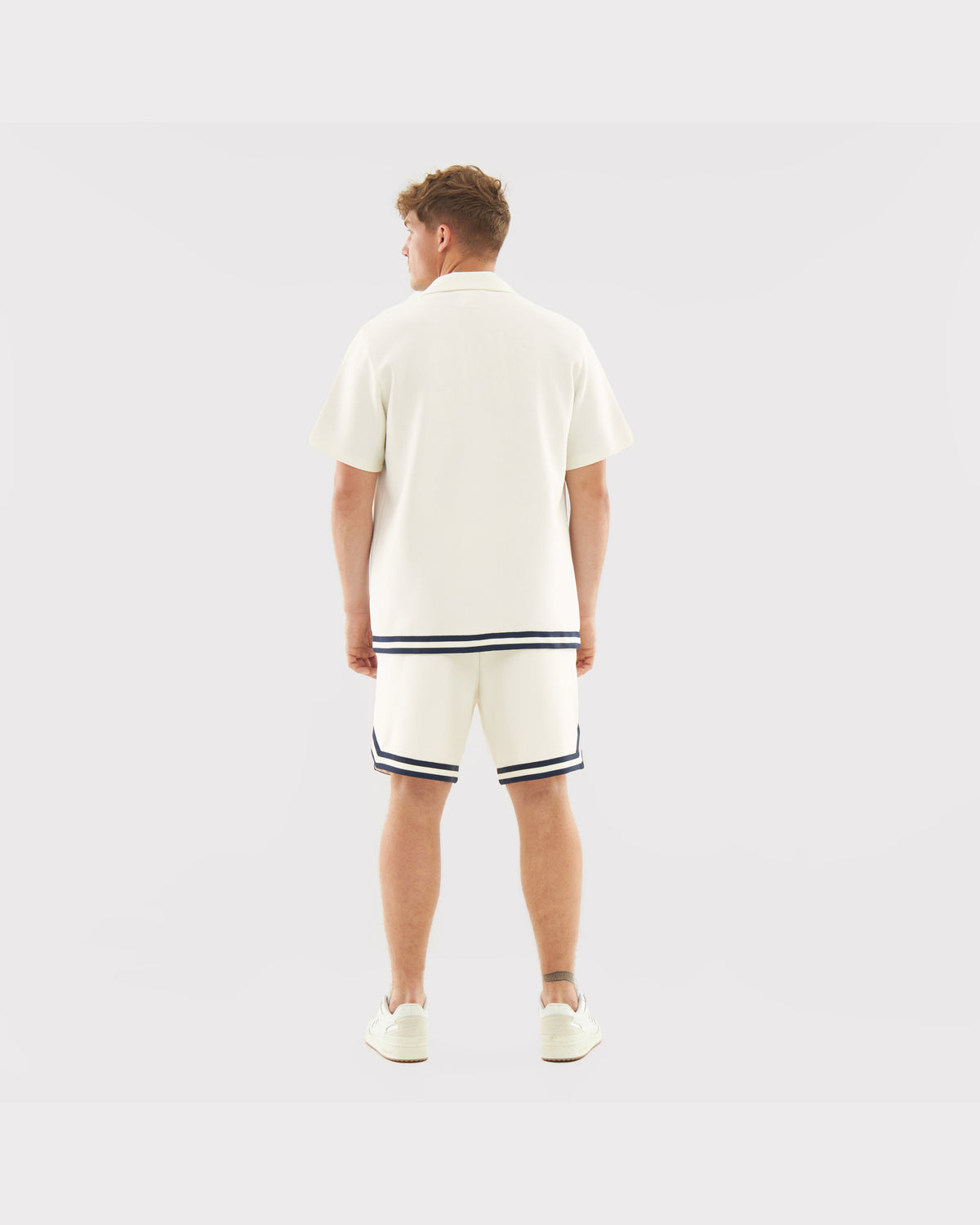 Mann trägt cremefarbenes Kurzarm-Set 'Parker' mit dunklen Streifen am Saum von Shirt und Shorts