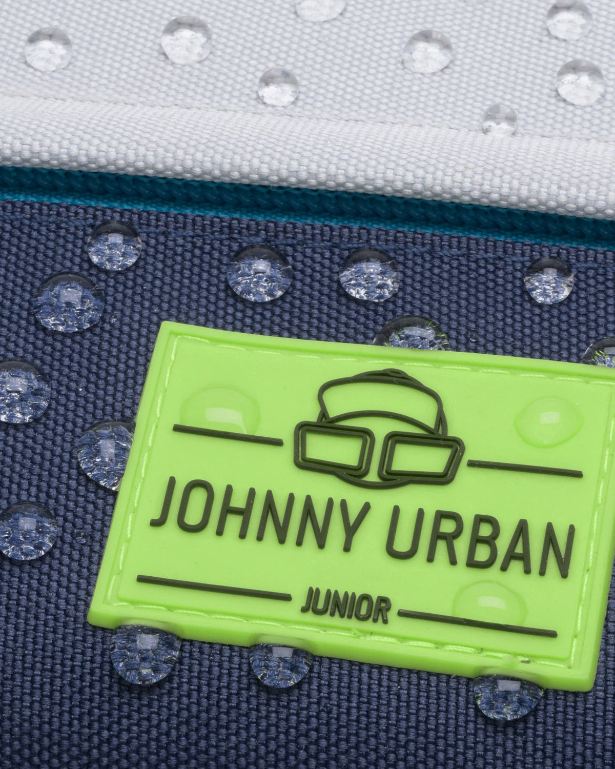 Grünes Johnny Urban Junior Logo auf wasserabweisendem blauem Stoff mit Wassertropfen