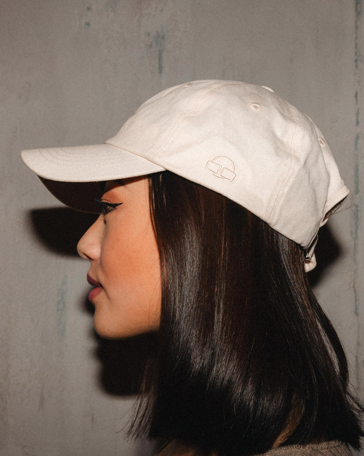 Beige Canvas Cap 'Jen' mit Logo, getragen von Frau im Profil vor grauer Wand