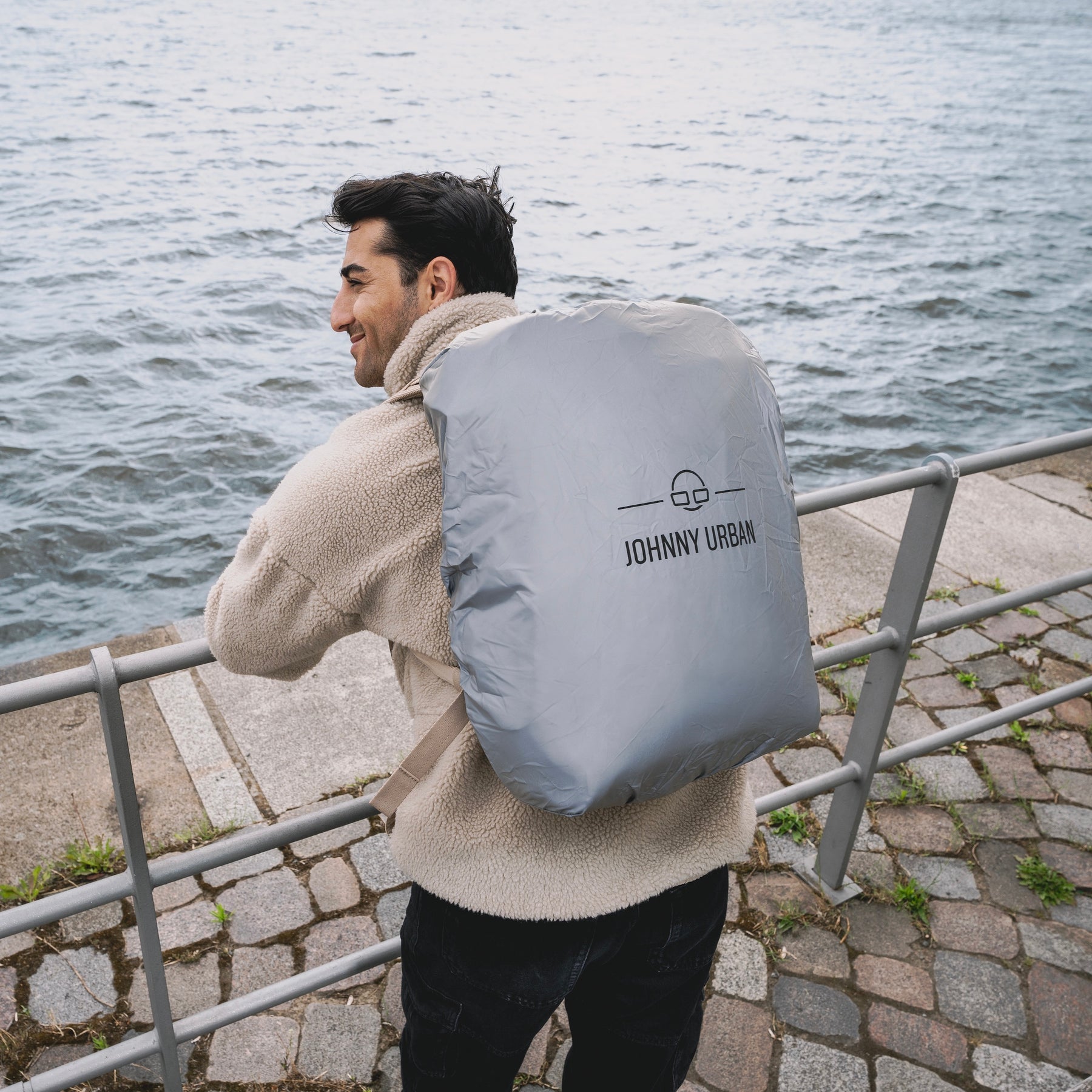 Person mit grünem Hoodie trägt silberne Regenschutzhülle 'Bo L' von Johnny Urban über dem Rucksack