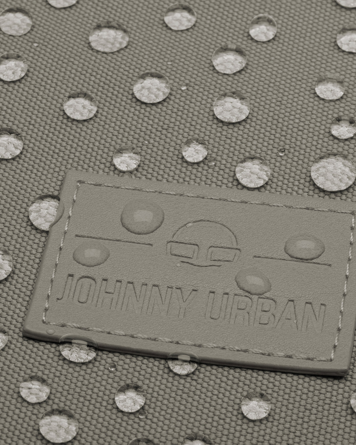 Nahe Aufnahme eines wasserdichten Johnny Urban Rolltop Rucksacks mit sichtbaren Wassertropfen auf dem grauen Gewebe