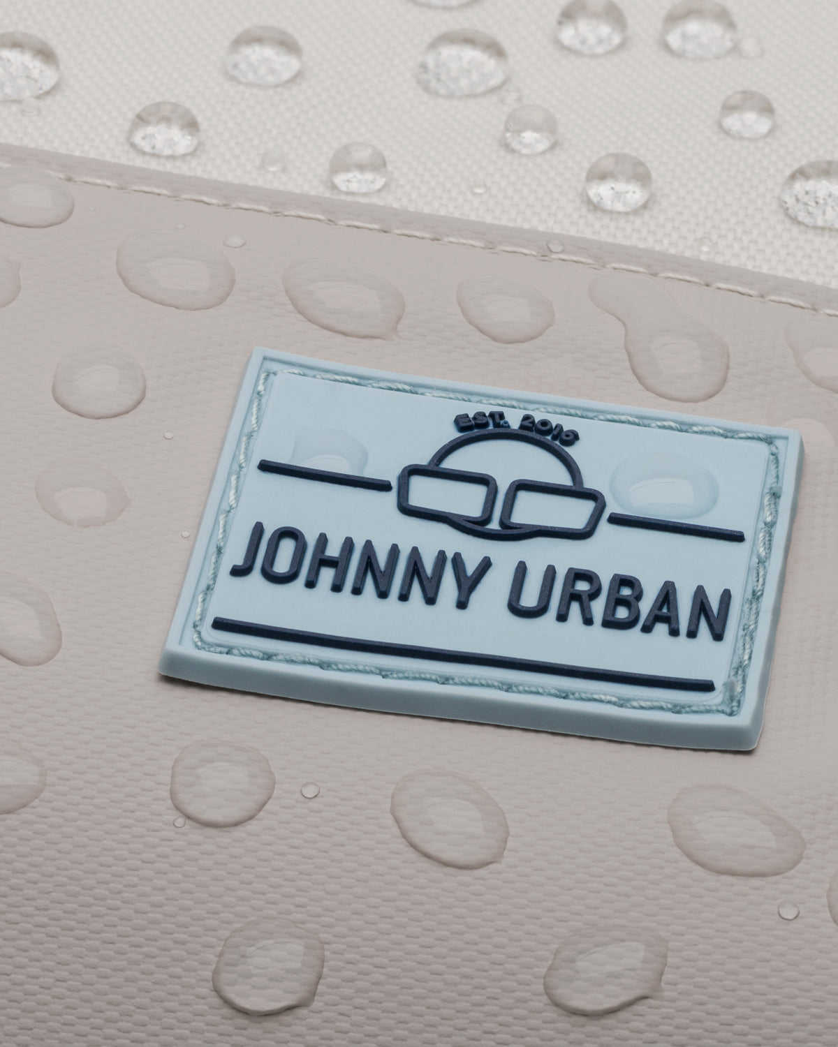 Nahaufnahme des wasserabweisenden Materials und des Johnn Urban Logos auf dem Rucksack 'Mika' in Beige