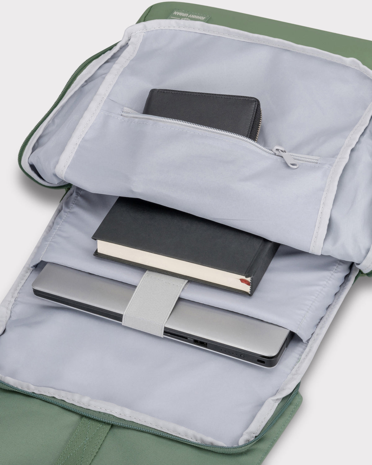 Geöffneter grüner Rucksack 'Mika' mit Laptopfach, einem Buch und einem Portemonnaie innen