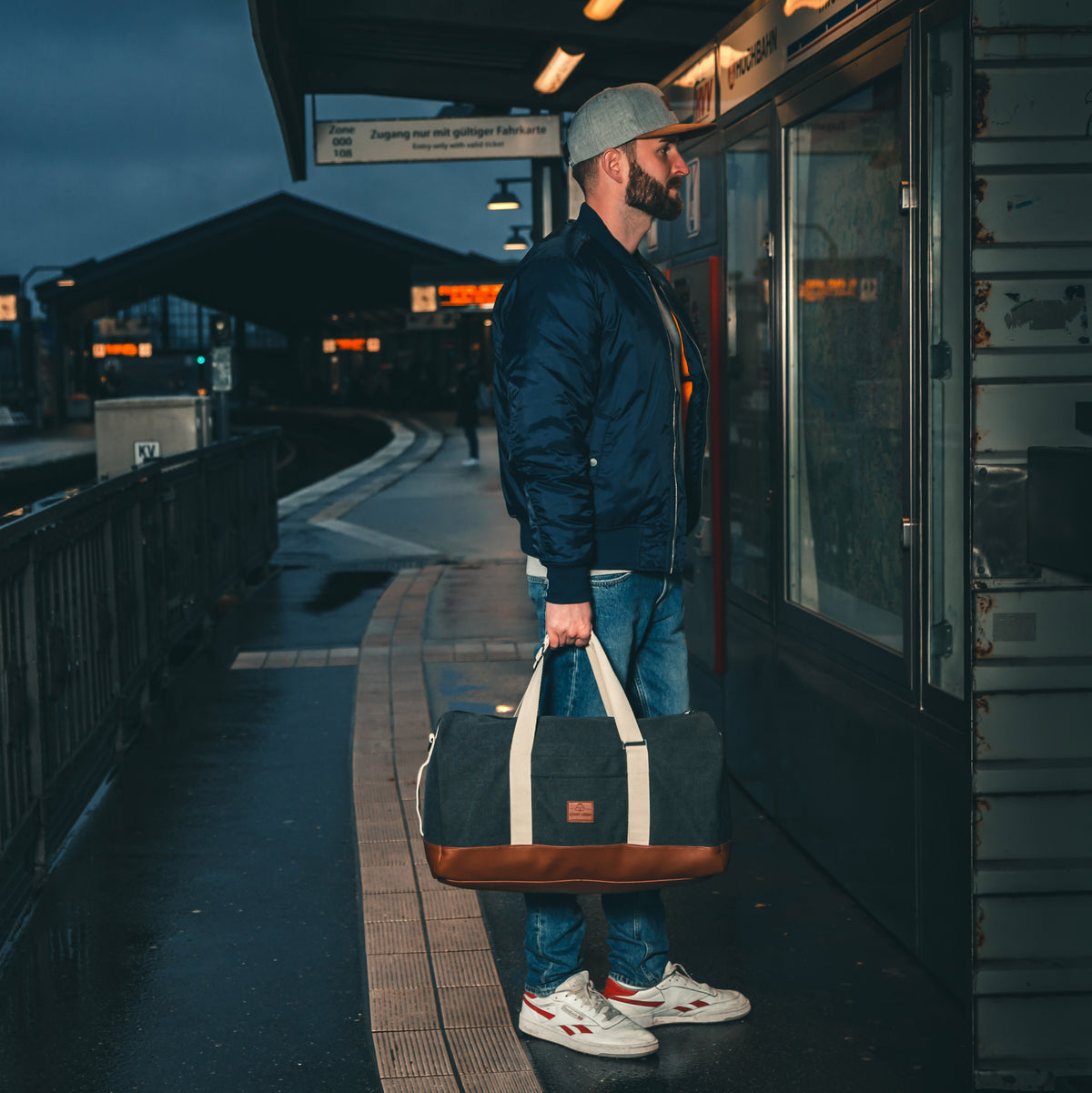 Mann am Bahnhof hält Weekender-Tasche 'Paul' in Anthrazit mit hellen Griffen und braunem Boden